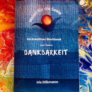 Könnte beinhalten: Ein blaues Arbeitsbuch mit dem Titel "DANKBARKEIT" und dem Text "Malen für die Seele" und "Ein kreatives Workbook". Das Cover zeigt ein stilisiertes Design mit einer roten und gelben Kugel über einer blauen Form. Der Name des Autors, Iris Dißmann, steht unten.