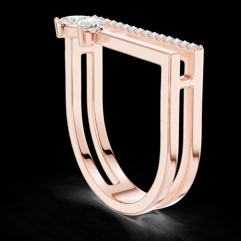 May include: Rose gold ring with a unique geometric design. The ring features a pear-shaped diamond and a row of smaller diamonds set along a rectangular bar. The ring's band has a double-layered, open design.