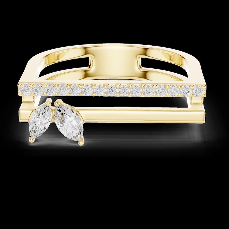 May include: A gold-colored ring with a rectangular design. The top section is adorned with a row of small, clear gemstones. Two marquise-cut gemstones are positioned on the lower section of the ring, adding a unique touch to the jewelry.