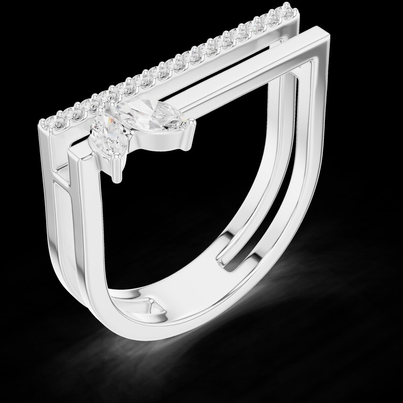 May include: A silver ring with a unique design. The ring features a row of small, clear stones along the top and two larger, marquise-cut stones. The band has a modern, open design.
