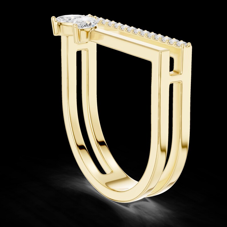 May include: A modern gold ring with a unique geometric design. The ring features a pear-shaped diamond and a row of smaller diamonds. The ring's band has a double-layered, open design, creating a bold and contemporary look.