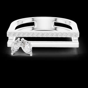 May include: A silver ring with a rectangular design, featuring a row of small, clear stones and two marquise-cut gemstones. The ring has a modern, geometric style and is set against a black background.