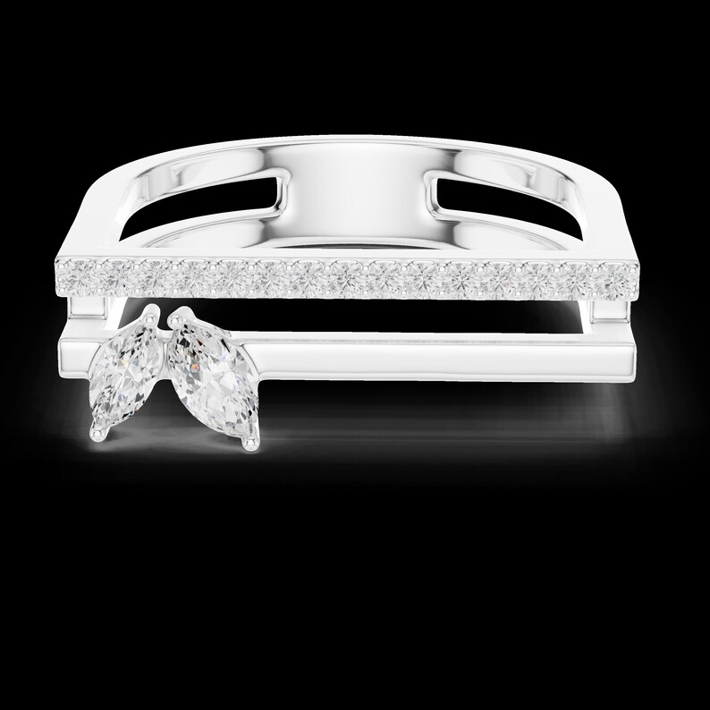 May include: A silver ring with a rectangular design, featuring a row of small, clear stones and two marquise-cut gemstones. The ring has a modern, geometric style and is set against a black background.