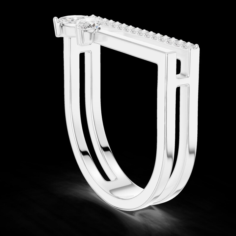 May include: A modern silver ring with a unique open design. The ring features a pear-shaped gemstone at the top and a row of small stones along the top bar. The ring's design is geometric and elegant, set against a black background.