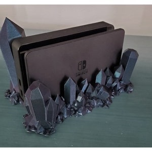 May include: A black Nintendo Switch console sits in a 3D printed stand made to look like a bed of dark, iridescent crystals.