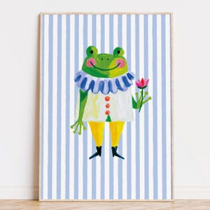 May include: A framed art print featuring a whimsical frog character. The frog is green with a white and blue ruffled collar, a white tunic with orange buttons, and yellow pants. It holds a pink flower against a blue and white striped background.