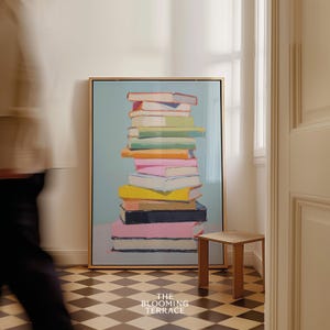 K&ouml;nnte beinhalten: Ein gerahmtes Gem&auml;lde eines Stapels bunter B&uuml;cher vor einem hellblauen Hintergrund. Das Gem&auml;lde ist in einem goldenen Rahmen und h&auml;ngt an einer wei&szlig;en Wand.