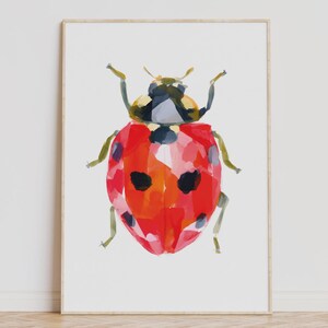 Puede incluir: Una pintura de acuarela enmarcada de una mariquita. La mariquita tiene un cuerpo rojo con manchas negras y una cabeza negra y gris. La pintura está sobre un fondo blanco y enmarcada en un marco de madera clara.
