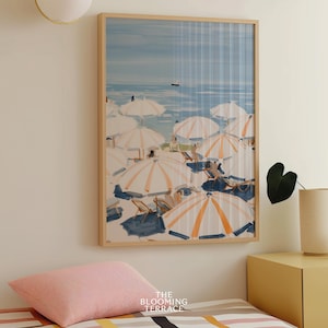 Beach scene featuring striped umbrellas and sunbathers by the calm ocean, painted in soft blue, peach, and cream tones — printable coastal wall art.