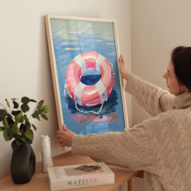 Digital painting of a pink and white lifebuoy floating on calm blue water. Bright and playful coastal art with summery, nautical vibes.