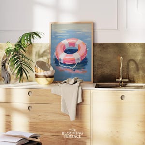 Digital painting of a pink and white lifebuoy floating on calm blue water. Bright and playful coastal art with summery, nautical vibes.
