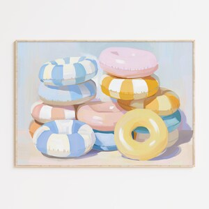 May include: A framed print featuring a stack of colorful inflatable rings. The rings are in various pastel colors, including pink, yellow, blue, and orange, with striped and solid designs. The artwork has a soft, painterly style, evoking a summery, beachy vibe.