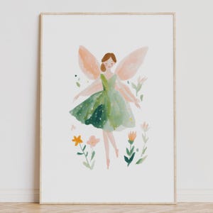 Op de afbeelding: Waterverfillustratie van een fee in een groene jurk met perzikkleurige vleugels, omringd door bloemen. De fee heeft bruin haar en glimlacht. Het kunstwerk is ingelijst in een licht houten frame.