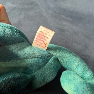 May include: A teal green beanie baby with a white tag that reads "Handmade in China", "1997 Ty Inc.", "Oakbrook, IL U.S.A.", "Surface Washable", "All New Material", "Polyester Fiber & PE Pellets", "CE", "Reg. No. PA 1965(KR)"