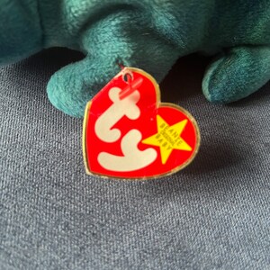 May include: Red Ty Beanie Baby tag with a white star and the text "Beanie Baby" in yellow. The tag is attached to a teal plush toy.