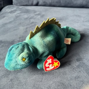 May include: Green and blue tie-dye beanie baby iguana with a yellow eye and a red Ty heart tag with a white star.
