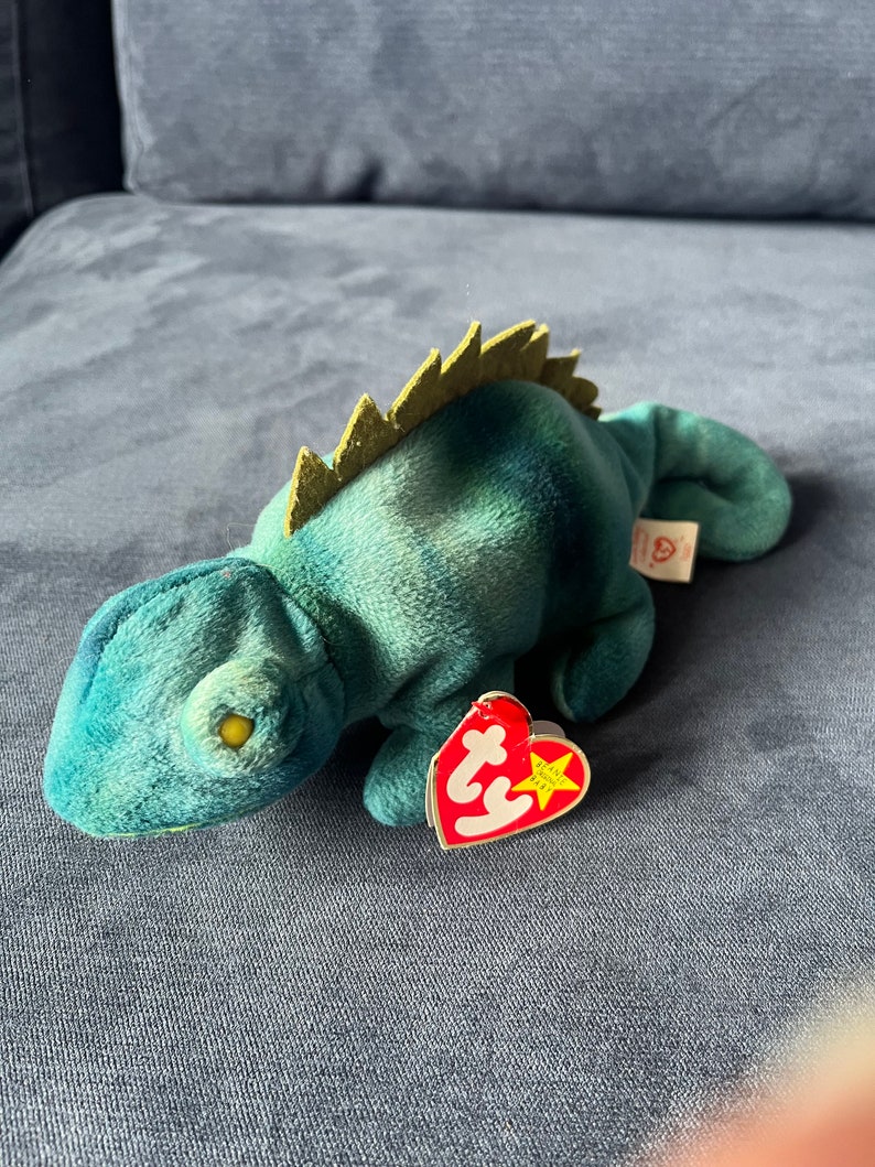 May include: Green and blue tie-dye beanie baby iguana with a yellow eye and a red Ty heart tag with a white star.