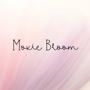 May include: A soft, layered tulle fabric in a gradient of pale pink to light lavender. The text 'Moxie Bloom' is centered in a thin, black, handwritten-style font over the textured, semi-transparent material that creates a delicate, airy effect.
