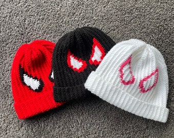Puede incluir: Tres gorros de punto con diseños de diferentes colores. Los gorros son rojo, negro y blanco. Cada gorro tiene un símbolo de Spider-Man blanco en la parte delantera.