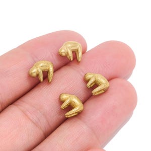 以下が含まれることがあります： ぶら下がった姿勢のナマケモノの形をした、4つの小さな金色の金属製チャーム。各チャームは滑らかな金属仕上げで、ナマケモノの頭、手足、体を定義する繊細な凹みがあり、グループとして配置されています。