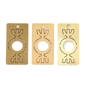 Puede incluir: Tres dijes rectangulares de metal con un diseño estilizado de un círculo con un tallo y hojas. Los dijes son de oro, latón y cobre.
