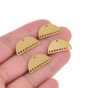 Pode incluir: Quatro componentes de joalharia em metal com tom de latão em forma de semicírculo, cada um com um orifício único no centro superior e uma fila de oito orifícios mais pequenos ao longo da borda inferior plana, dispostos em leque numa palma.