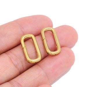 May include: Two gold-toned metal oval spring gate rings with a smooth, polished finish. Each ring features a hinged opening mechanism on one side, allowing the loop to be opened and closed securely for connecting various items or accessories.