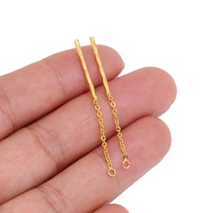 May include: A pair of gold-toned earrings featuring a straight, textured metal bar attached to a delicate link chain. Each earring ends in a small circular loop, providing a simple and clean design for jewellery making or accessory customisation.