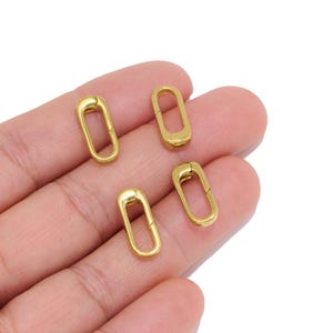 May include: Four small, oval-shaped gold-toned metal spring gate rings. Each piece features a smooth, polished finish and a functional hinged mechanism that allows the ring to open and close securely for connecting jewelry components or charms.