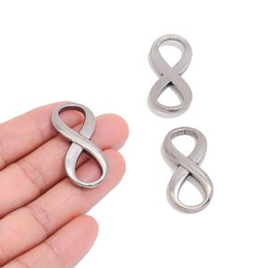 May include: Three silver-toned metal infinity symbols with a smooth, polished finish. Each piece features a continuous, looped design forming the mathematical symbol for infinity. The objects are solid, reflective, and have a rounded contour.