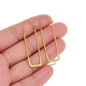 May include: A pair of gold-toned earrings featuring a long, thin, rectangular wire frame design. Each earring has a curved hook closure at the top, creating a continuous, open geometric shape that hangs vertically with a smooth, metallic finish.