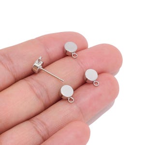May include: Four silver-toned metal earring studs with a flat circular top and a small attached loop at the base for hanging charms. Each stud features a smooth, reflective surface and a thin post extending from the back for secure attachment.