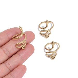 May include: Three gold-toned metal rings, each shaped like a coiled snake. One ring is positioned on a palm, while two additional identical rings are placed separately. The snake design features a smooth, polished finish with a curved, wrap-around band.