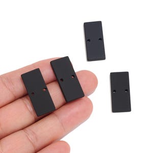 Peut inclure: Trois petits composants rectangulaires noir mat, chacun doté de deux trous circulaires positionnés au centre sur la longueur. Ces pièces plates de couleur unie présentent des coins arrondis et une finition lisse et uniforme pour divers usages.