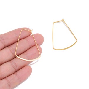 May include: A pair of gold-toned hoop earrings featuring a distinct trapezoidal shape with a curved bottom edge. The earrings are constructed from thin, delicate wire and include a standard post-back closure mechanism for secure attachment.