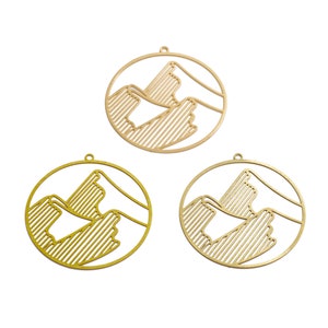 May include: Three gold-colored metal charms in the shape of a circle with a mountain range design inside.