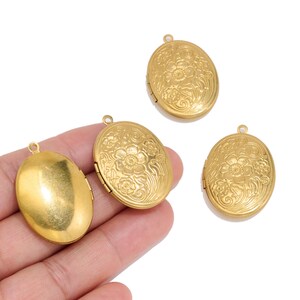 May include: Three oval-shaped gold-colored metal lockets. Two of the lockets feature an embossed floral pattern on the front surface, while one locket has a smooth, plain surface. Each locket includes a small metal loop at the top for attachment.