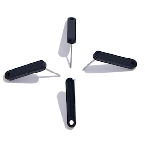 May include: Four black stud earrings arranged in a cross pattern. Each earring features a long, narrow, rounded rectangular black top piece with a small circular hole at one end and a thin, straight silver-toned metal post extending from the back.