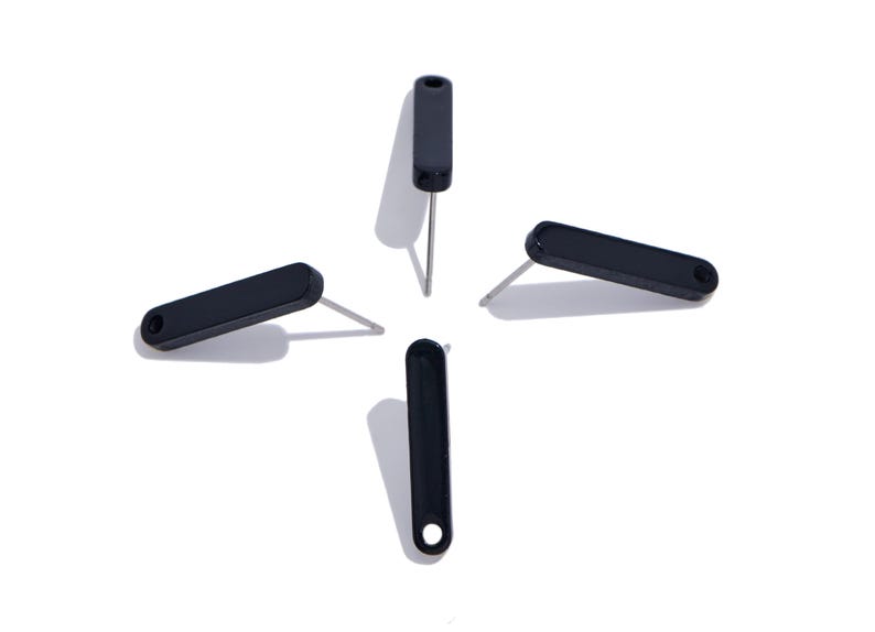 May include: Four black stud earrings arranged in a cross pattern. Each earring features a long, narrow, rounded rectangular black top piece with a small circular hole at one end and a thin, straight silver-toned metal post extending from the back.