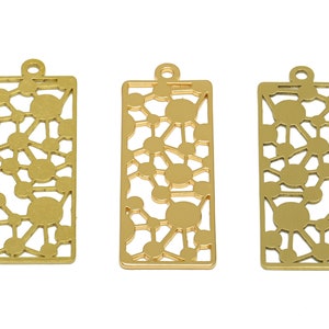 May include: Three gold-colored metal charms with a geometric pattern of circles and lines. The charms are rectangular and have a hole at the top for hanging.