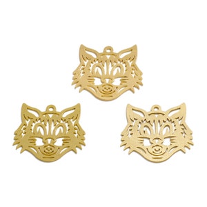 Op de afbeelding: Drie gouden metalen kattengezicht bedels met een uitgesneden ontwerp. De bedels hebben een gat aan de bovenkant om op te hangen.
