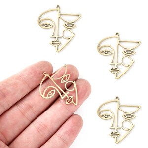 K&ouml;nnte beinhalten: Vier goldfarbene Metall-Anh&auml;nger in Form von abstrakten Gesichtern. Jeder Anh&auml;nger zeigt eine stilisierte Umrandung eines Gesichts mit zwei Augen, einer Nase und einem Mund.