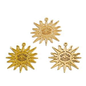 May include: Three gold-colored metal sun charms with an eye design in the center. Each charm has a pointed starburst shape with a loop at the top for hanging.