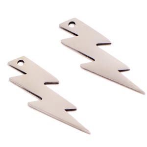 Pode incluir: Dois pingentes prateados em forma de raio. Cada pingente tem um furo na parte superior para enfiar. O design do raio é uma forma clássica, com ângulos agudos e uma parte inferior pontiaguda.