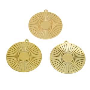 May include: Three gold-colored, circular pendants with a sunburst design. Each pendant features a central circle with radiating lines, and a small loop at the top for hanging. The pendants are likely for jewelry making or crafting.