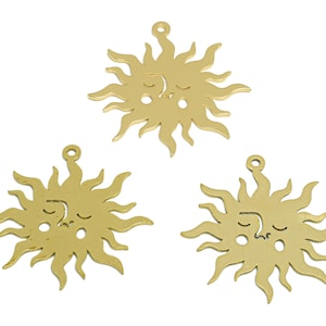 May include: Three gold-colored metal sun charms with a face design. Each charm has a loop at the top for attaching to a necklace or bracelet.