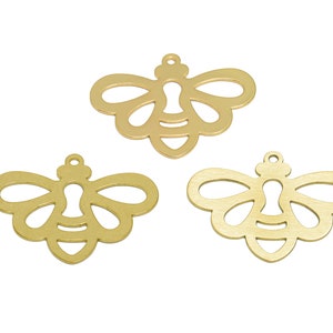 May include: Three gold metal bee charms with a cutout design. The bees have a keyhole shape in the centre.