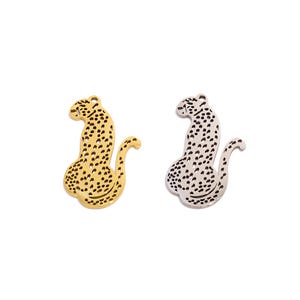 Puede incluir: Dos dijes de leopardo de metal, uno dorado y otro plateado, con un diseño de puntos detallado.