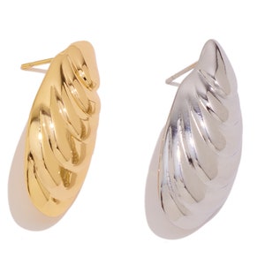 Puede incluir: Un par de pendientes, uno dorado y otro plateado, con un diseño texturizado con forma de concha.