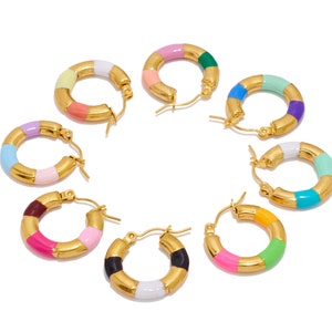 May include: Eight pairs of gold hoop earrings with colorful enamel accents. Each hoop earring has a different color combination of pink, blue, green, yellow, white, and black.
